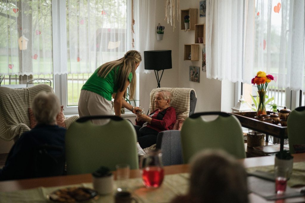 Cuidador ayudando a mujeres mayores con el té en un entorno acogedor de residencia de ancianos.